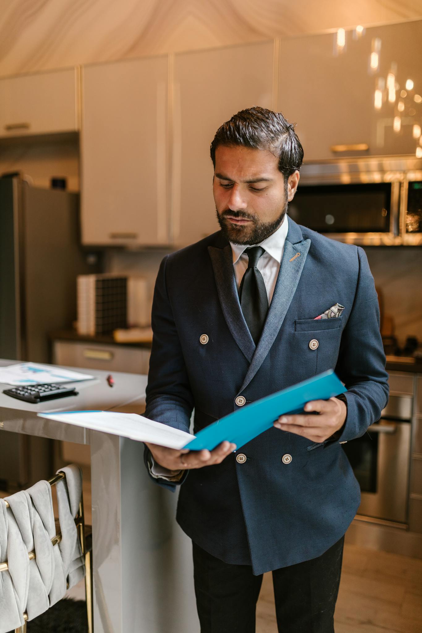 A stylish adult businessman in a suit reading documents in a modern kitchen setting.