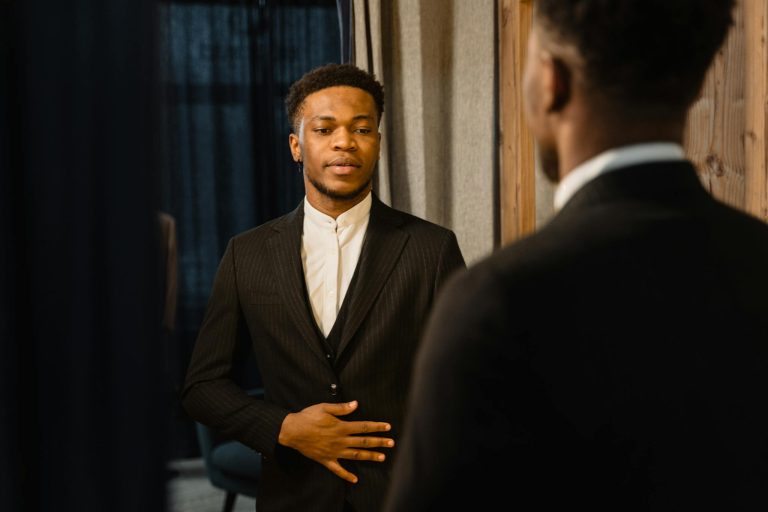 Elegant man in a stylish suit looking at his reflection in an indoor setting, exuding confidence.
