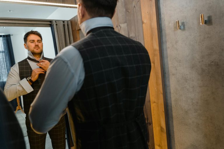 Stylish adult man adjusts his suit in the mirror, depicting fashion and elegance indoors.